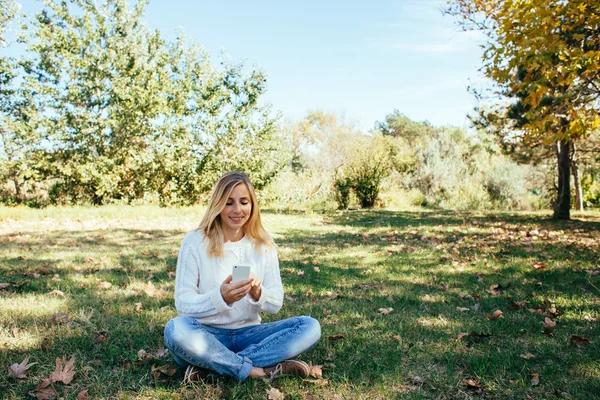 Young woman sitting in the park and using her cell phone. woman sending a text message from her mobile phone outdoor