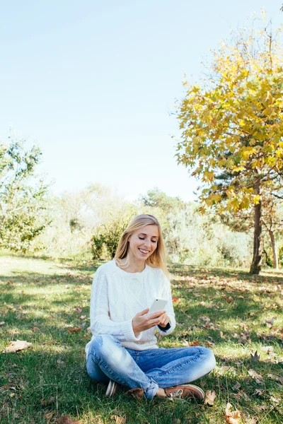 Young woman sitting in the park and using her cell phone. woman sending a text message from her mobile phone outdoor