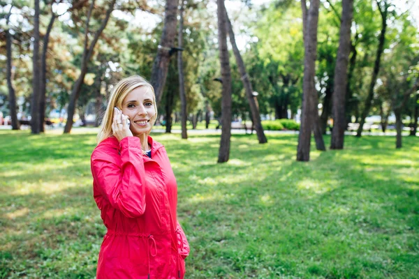 Young blonde woman in a pink jacket talking on the phone. Woman using smart phone outdoor