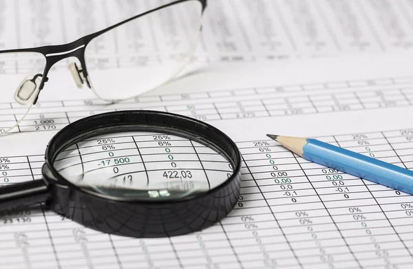 Business research. Closeup of spectacles magnifying glass and pencil on paper with digits