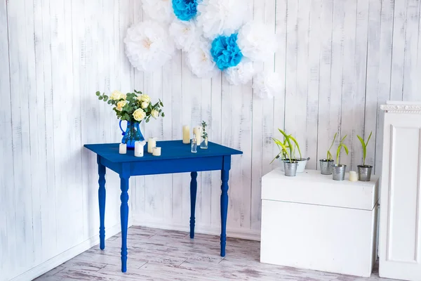 Interior design, white flowers, roses in a blue vase on a blue table with a white wooden background.