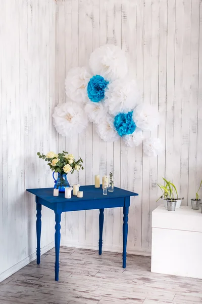 Interior design, white flowers, roses in a blue vase on a blue table with a white wooden background.