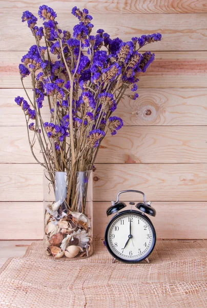 Clock with violet flower on wood background