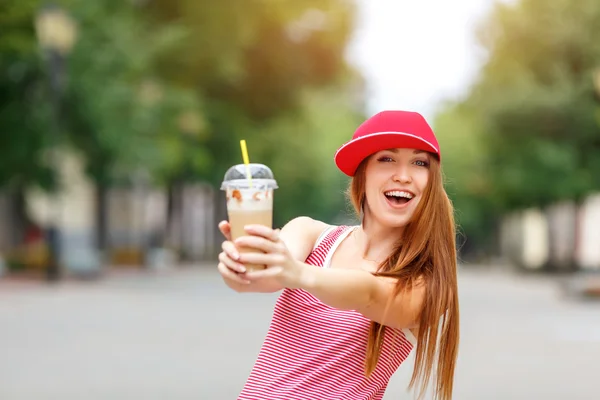 Fashion city portrait of stylish hipster woman with milk shake, red striped dress, red cap and sneakers, makeup, long brunette hairs, walking alone at weekend, enjoy vacation in Europe, modern trendy