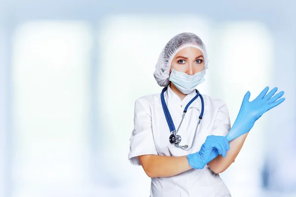 Medical surgeon doctor woman over blue clinic background. Doctor putting on sterile gloves. Place for medical advertise. Medical advertising concept.