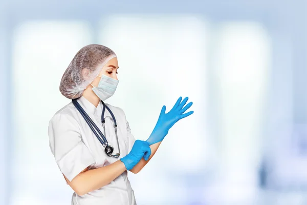 Medical surgeon doctor woman over blue clinic background. Doctor putting on sterile gloves. Place for medical advertise. Medical advertising concept.