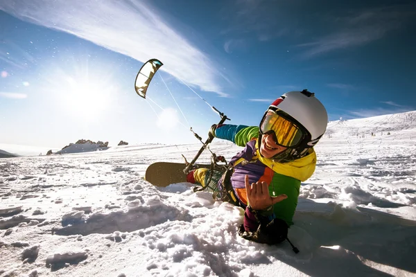 Happy snowboarder lies and holds snowkite