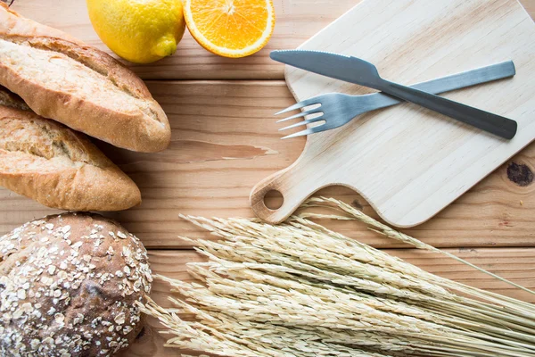 Baguette bread and whole wheat bread with fruit on wooden background.