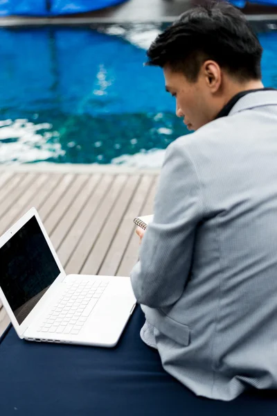 Businessman working with laptop computer at swimming pool.