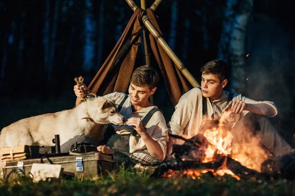 Two twin brothers sitting around a campfire