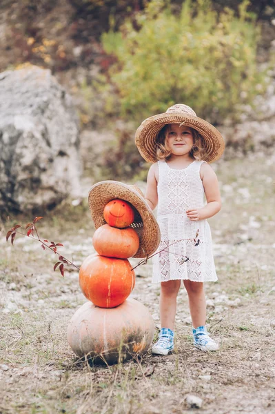 Little girl in a straw hat by pumpkins