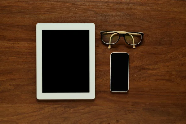 Top view of tablet computer, smartphone and glasses on wooden ta