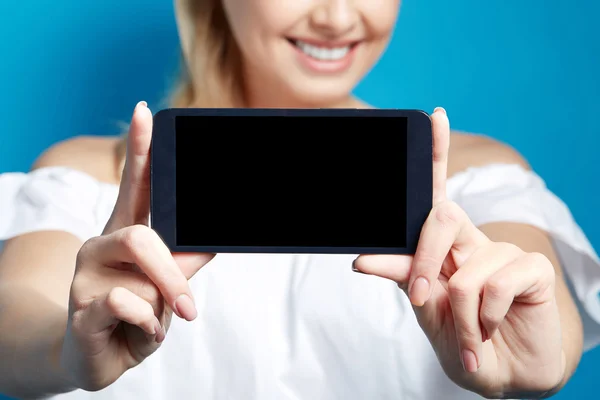 Young smiling woman showing screen of phone on blue background.