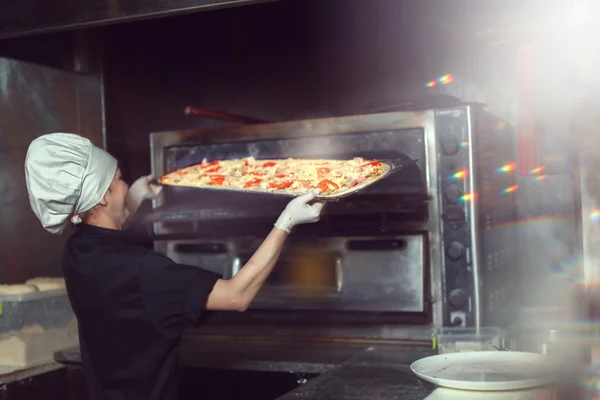 Chef baker cook in black uniform putting pizza into the oven with shovel at restaurant kitchen