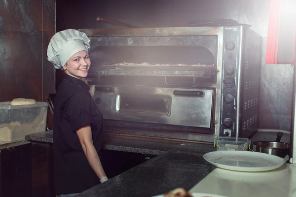 Chef baker cook in black uniform putting pizza into the oven with shovel at restaurant kitchen