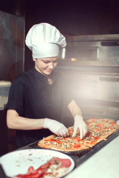 Chef baker cook in black uniform putting pizza into the oven with shovel at restaurant kitchen