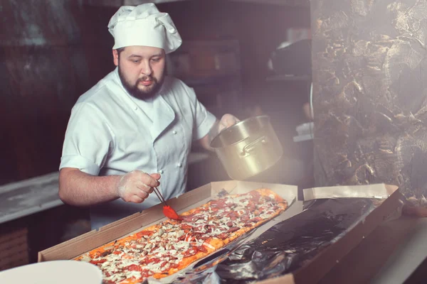 Chef baker cook in black uniform putting pizza into the oven with shovel at restaurant kitchen