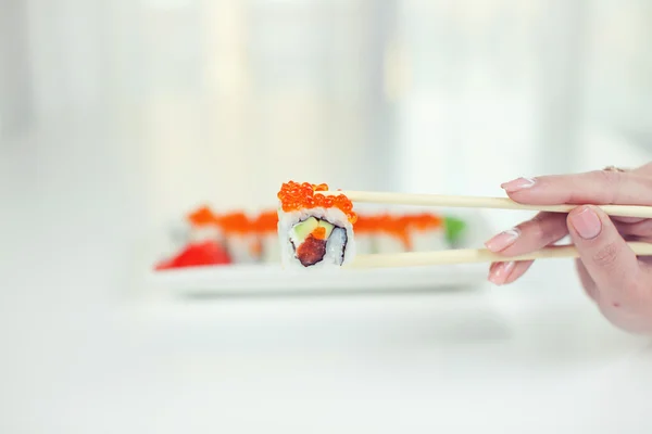 Close up of chopsticks taking portion of sushi roll on the table restaurant / eating sushi roll using chopsticks