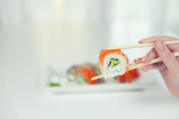 Close up of chopsticks taking portion of sushi roll on the table restaurant / eating sushi roll using chopsticks
