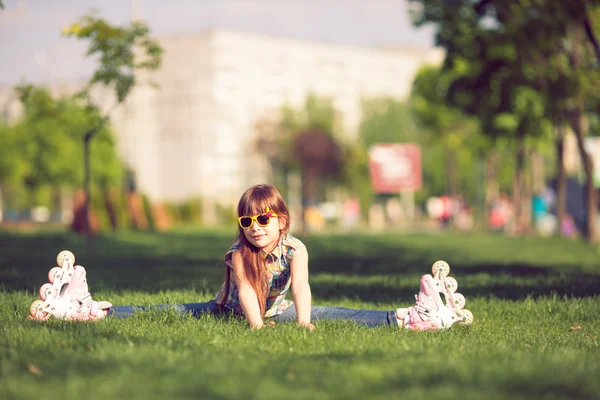 Girl wearing roller skates sitting on grass in the park.