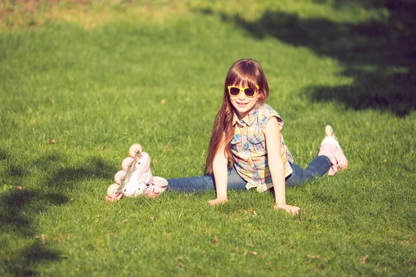 Girl wearing roller skates sitting on grass in the park.