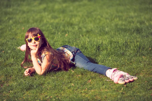 Girl wearing roller skates sitting on grass in the park.