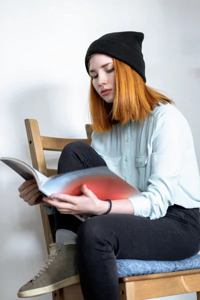 Red-haired girl leafing through a magazine.