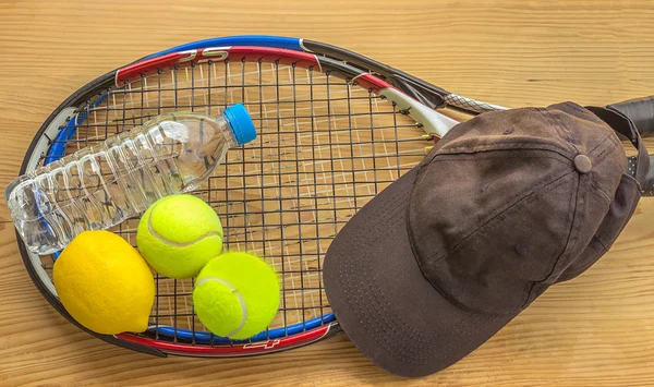 Tennis rackets and balls are next to a bottle of water, lemon,