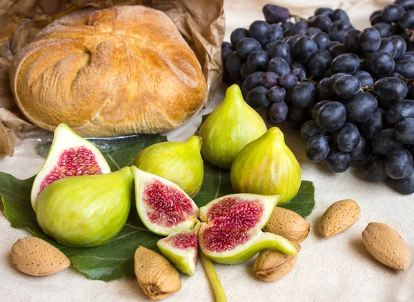 Still life of fresh colorful fruits. Bunch of black grapes, green figs on a light background. Bread in the package of paper.