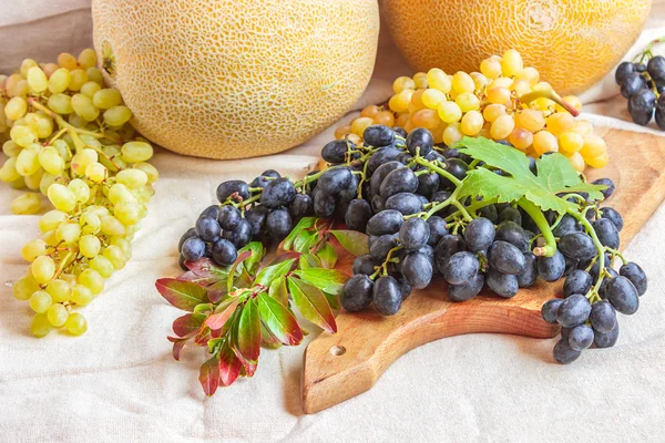 Still life - bright fruit on light fabric. Vintage black and green grapes, melon and pomegranate branch.