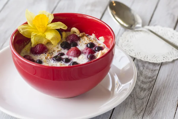 Red bowl of cereal with strawberries with berries on wood background