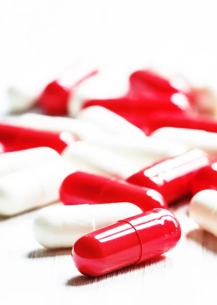 Red and white tablets in capsules on a white wooden background