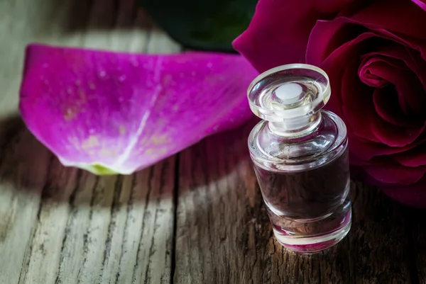 Rose essential oil in a small bottle and pink rose