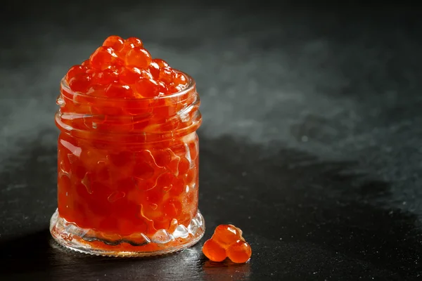 Red caviar in a glass jar on black stone background