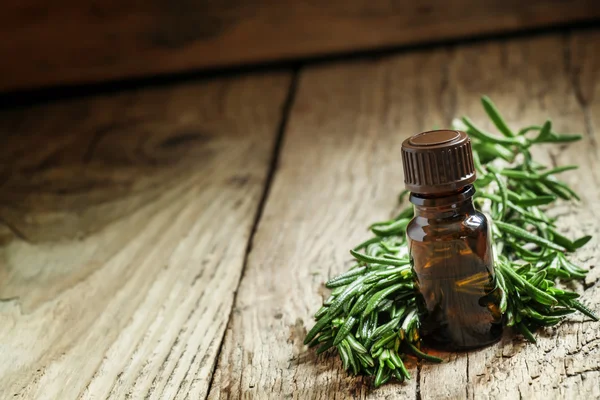Rosemary essential oil in a small bottle and fresh rosemary