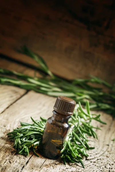 Rosemary essential oil in a small bottle and fresh rosemary
