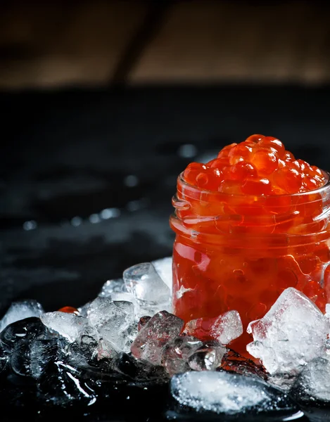 Delicious red caviar in a glass jar on crushed ice