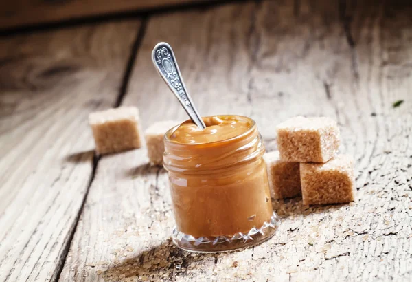 Sweet liquid caramel in a small jar and brown cane sugar