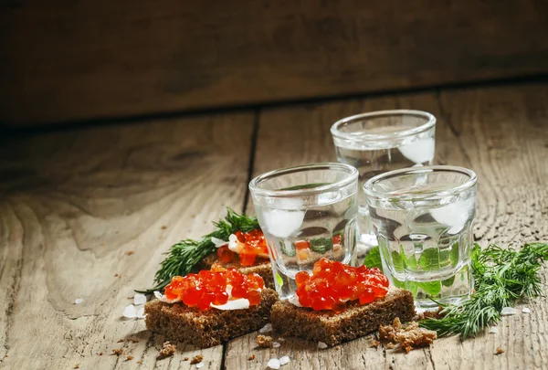 Cold Russian vodka with ice and small snacks sandwiches with caviar