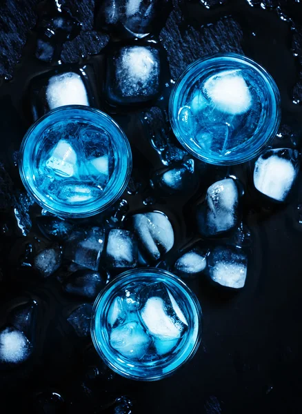 Blue cocktail with ice cubes on black stone background