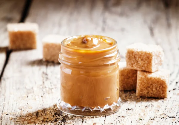 Sweet liquid caramel in a small jar and brown cane sugar