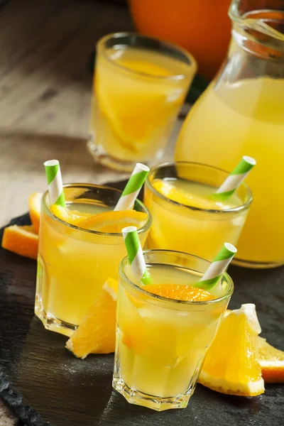 Orange drink in small glasses with striped straws and pitcher