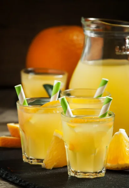 Orange drink in small glasses with striped straws and pitcher