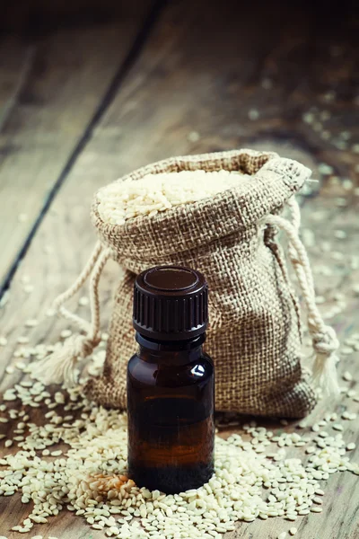 Essential sesame oil in a bottle of brown glass and sesame seeds