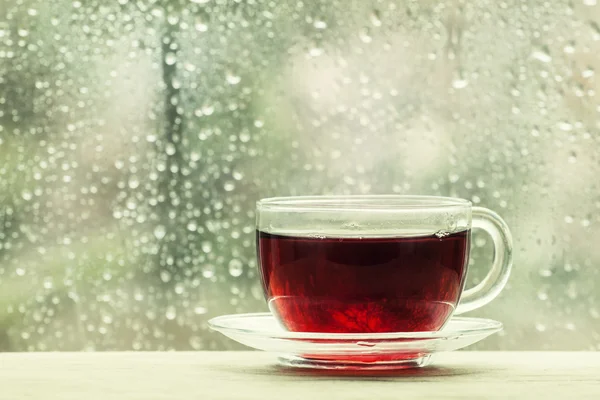 Cup of hot black tea on the blurred background of wet window