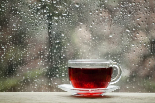 Cup of hot black tea on the blurred background of wet window