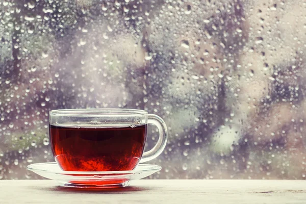 Cup of hot black tea on the blurred background of wet window