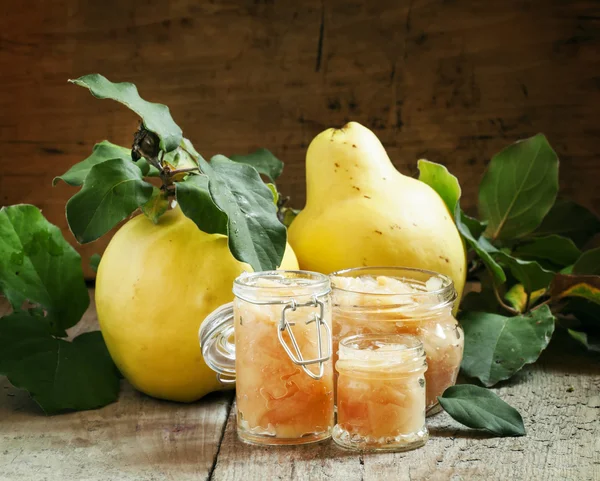 Pink quince jam in glass jars and fresh quince fruits with leaves