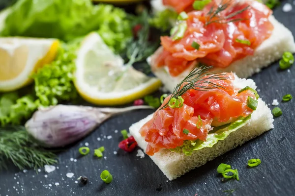 Small sandwiches with salty salmon,  soft cheese and green salad