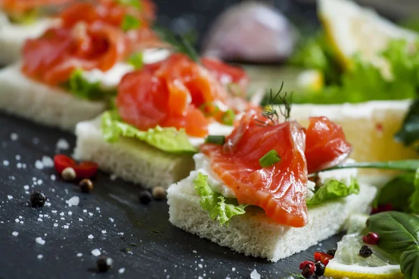 Small sandwiches with salty salmon,  soft cheese and green salad